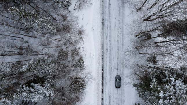 An aerial photo of a car driving on a snow-covered road. 