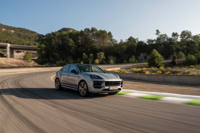 A silver 2024 Porsche Cayenne Turbo E-Hybrid coupe drives swiftly on a track