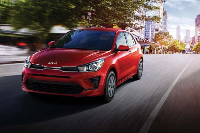 A red Kia Rio hatchback driving down a city street