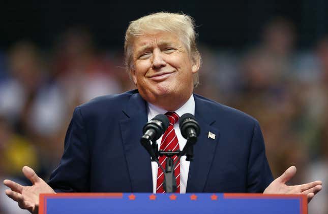 Trump smirking and holding his hands up at a podium during a rally