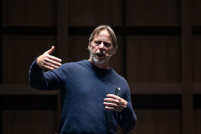 Jim Keller wearing a navy sweater speaking on stage doing a motion with his hands