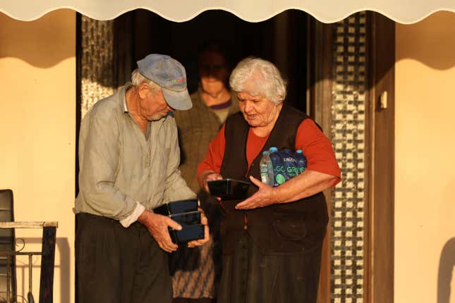 An elderly couple holds food and bottles of water in the flooded town of Palamas, near Karditsa, Thessaly region, central Greece, Friday, Sept. 8, 2023. Rescue crews in helicopters and boats are plucking people from houses in central Greece inundated by tons of water and mud after severe rainstorms caused widespread flooding. (AP Photo/Vaggelis Kousioras)