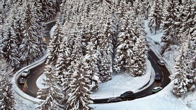 A photo of cars driving along a snow-covered hairpin bend. 