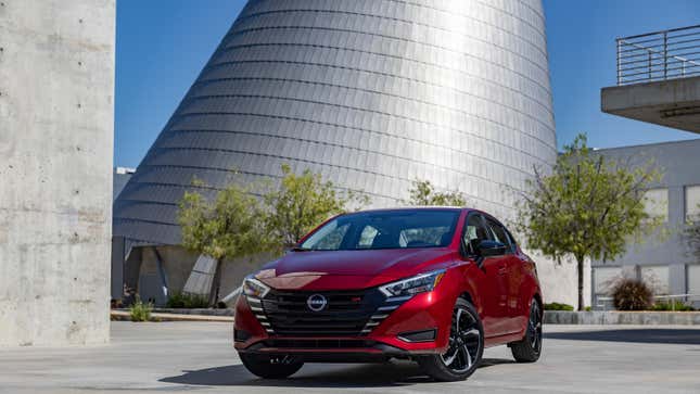 A red Nissan Versa parked in front of a big silver architectural structure