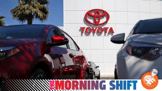 A Toyota logo on a dealership viewed between two cars on the lot.