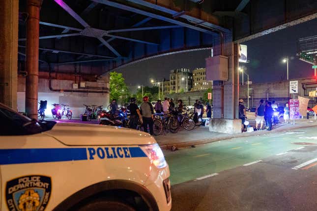 Police officers sit in their patrol car next to a group of delivery workers gathering to cross the Willis Avenue Bridge on July 15, 2021 in New York City. 