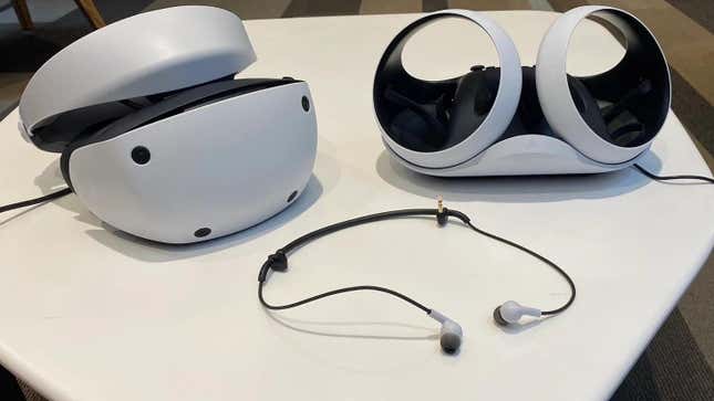 A PSVR2 headset with the two controllers and the attached earbuds.