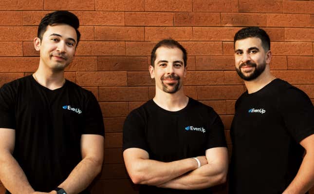 three men stand together in front of a brick wall all wearing black t-shirts that say EvenUp