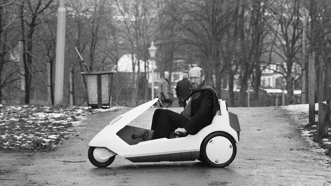 A black and white photo of Clive Sinclair in a C5 small EV. 