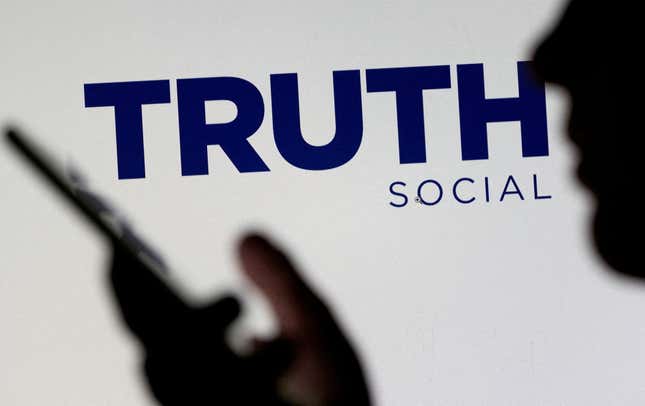  The Truth social network logo is seen displayed behind a woman holding a smartphone