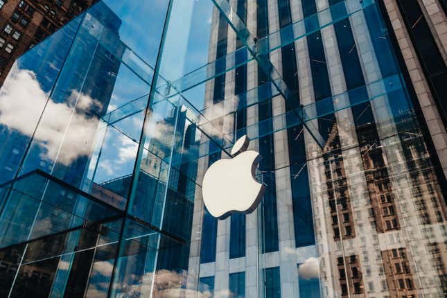 صورة للجدران الزجاجية الشاهقة لمتجر Apple Store، مع انعكاس مباني المدينة والسحب على ألواحها.