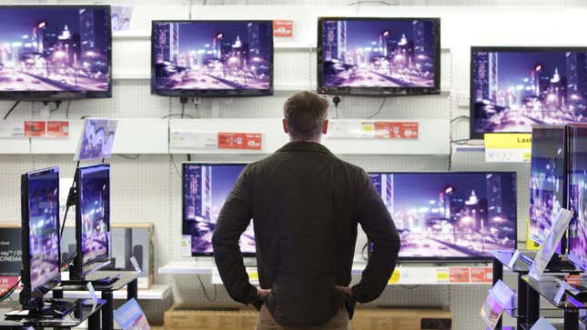 A photo shows a man looking at a lot of TVs in a store. 