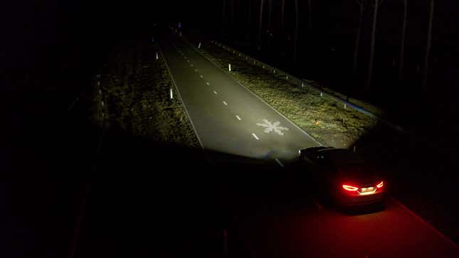 Car driving at night with headlights projecting a snowflake on the road.