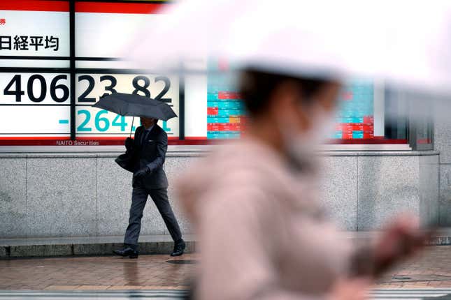 A person walks in front of an electronic stock board showing Japan&#39;s Nikkei 225 index at a securities firm in the rain Monday, March 25, 2024, in Tokyo. Asian shares were trading mixed on Monday, as investors awaited further indications the Federal Reserve might begin cutting interest rates.(AP Photo/Eugene Hoshiko)