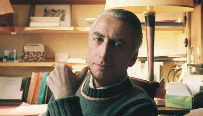 Roland Barthes, in a green sweater, holding a cigarette.