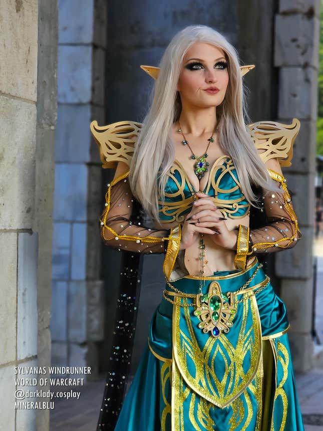 A cosplayer dressed as Sylvanas from World of Warcraft stands with hands clasped and eyes upward.