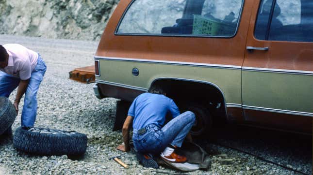 a photo of two people working on the back passenger tire of an old Suburban