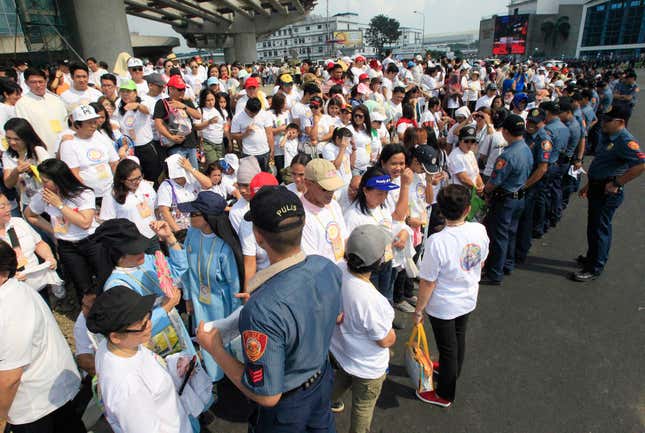 Members of the Philippine National Police (PNP) stand guard in front of well-wishers waiting along a main street for the arrival of Pope Francis in Manila