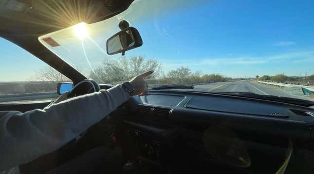 Someone points out of the windshield of a car driving on a two-lane highway