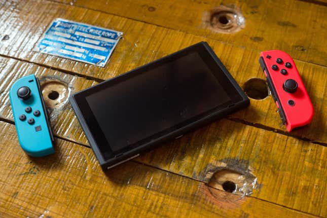 A Nintendo Switch sits atop a wooden surface with its detached wireless Joy-Con controllers next to it.