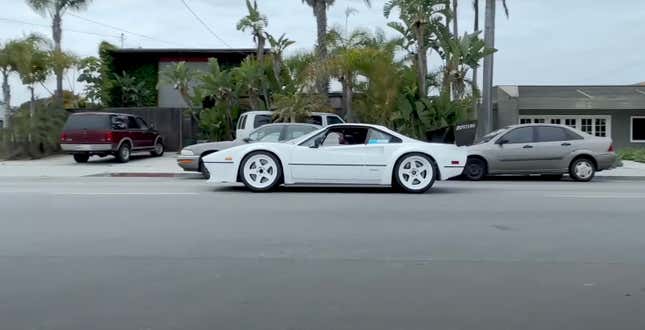 A white Ferrari race car drives on the street. It has white wheels.