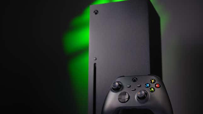An Xbox and a controller stand in front of a green lit background.