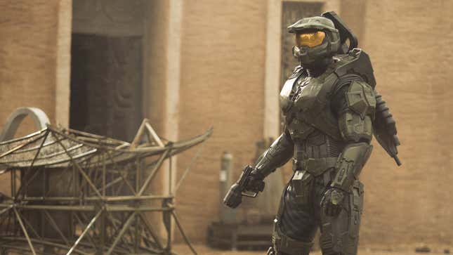 Master Chief examines a battlefield, holding his pistol out at his side.
