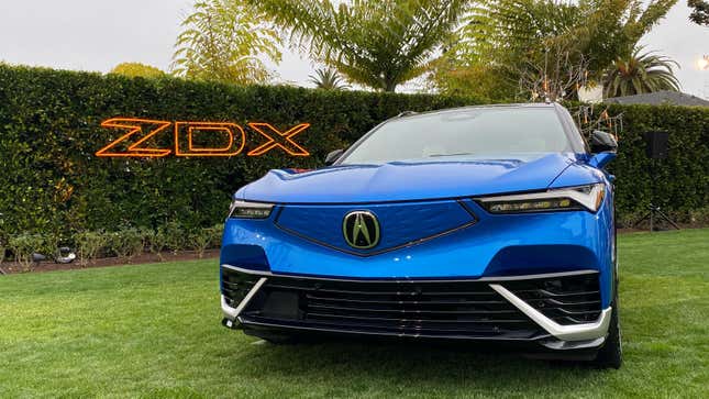 A front view of a blue ZDX Type S parked on grass in front of a hedge with an orange ZDX sign hung on it
