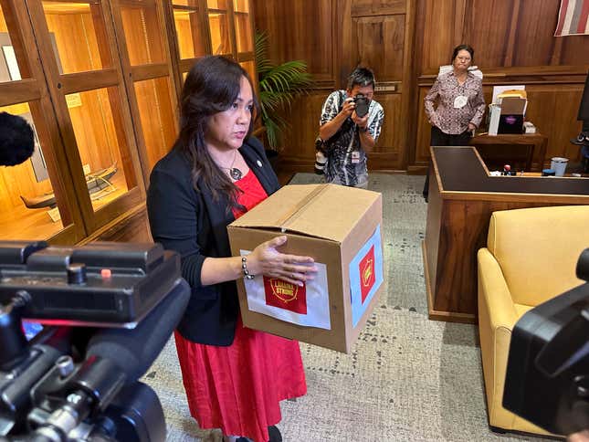 Bonnelley Pa&#39;uulu, the director of constituent services for Hawaii Gov. Josh Green, accepts a box on Tuesday, Oct. 3, 2023, with a petition asking Hawaii Gov. Josh Green to delay plans to reopen a portion of West Maui to tourism starting this weekend. The petition signed by more than 14,000 people comes amid a fierce and anguished debate over when travelers should return to the region, home to the historic town of Lahaina that was destroyed in the deadliest U.S. wildfire in more than a century. (AP Photo/Audrey McAvoy)