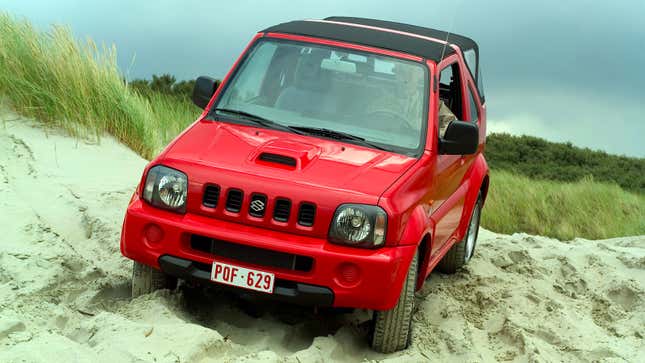 A photo of a red Suzuki Jimny SUV driving over sand. 