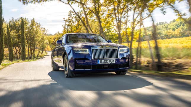 A purple Rolls-Royce Ghost driving down a tree-lined road.