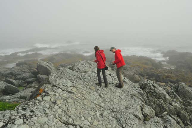 two people wearing red rain jackets standing on a rocky cliff overlooking other rocky land and water