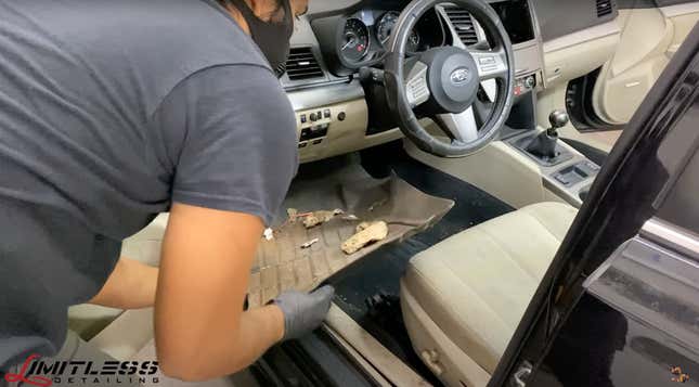 Man in a gray shirt cleaning a very dirty car with tan interior