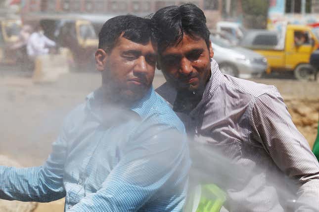 A man sprays two men on a motorcycle in Karachi.