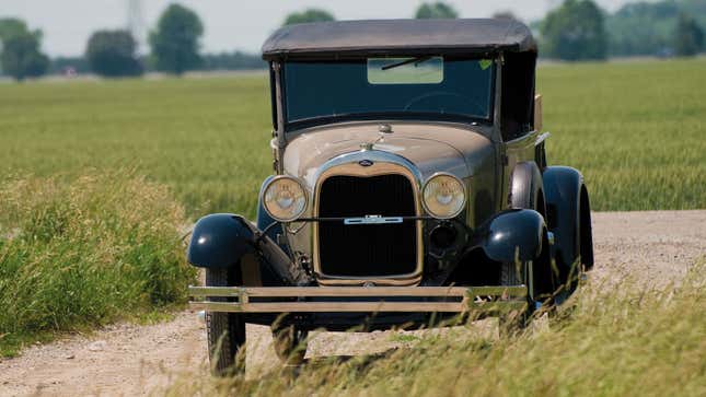 A photo of a brown, vintage Ford car driving down a dirt road. 