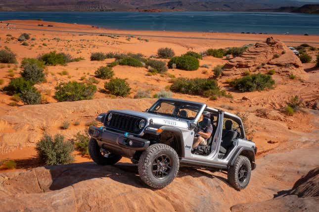 Cette photo montre un Jeep Wrangler hybride sans toit ni portes gravissant une pente surplombant un lac.