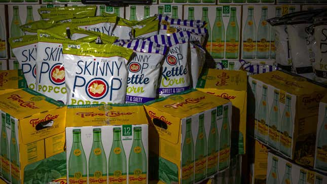 Cases of Topo Chico seltzer and Skinny Pop popcorn in a darkened grocery store.