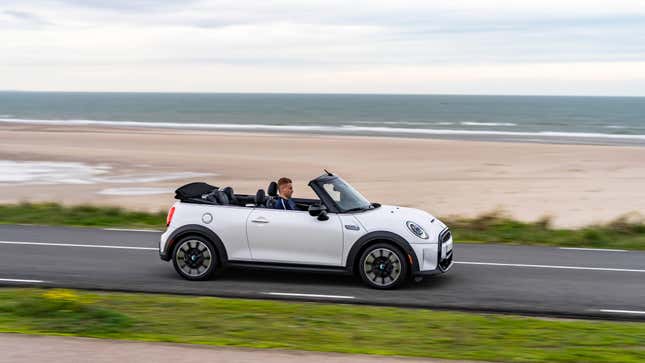 A white Mini Cooper S Convertible driving on a road next to the beach