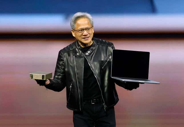 Jensen Huang holding up a small gold-colored super computer in one hand and a laptop in the other as he speaks on stage wearing his signature black leather jacket