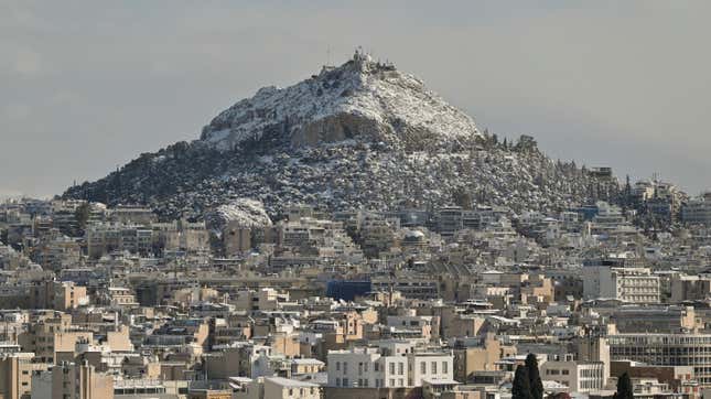 Snow-covered Lycabettus Hill in Athens. A cityscape sits in the foreground.