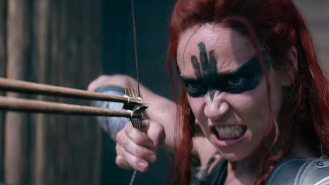 Red Sonja grimaces as she prepares to fire two arrows from a bow.