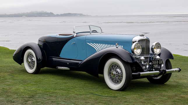 A photo of a blue and black vintage car by the sea. 