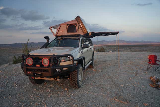 A Ford Ranger is set up for camping in the desert. An awning extends from the side.