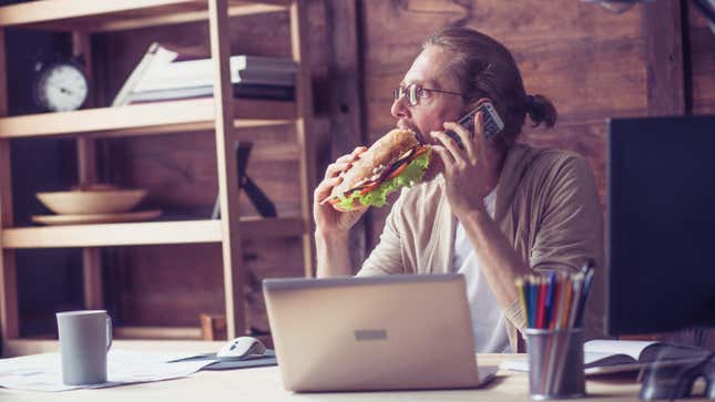 man eating sandwich at desk