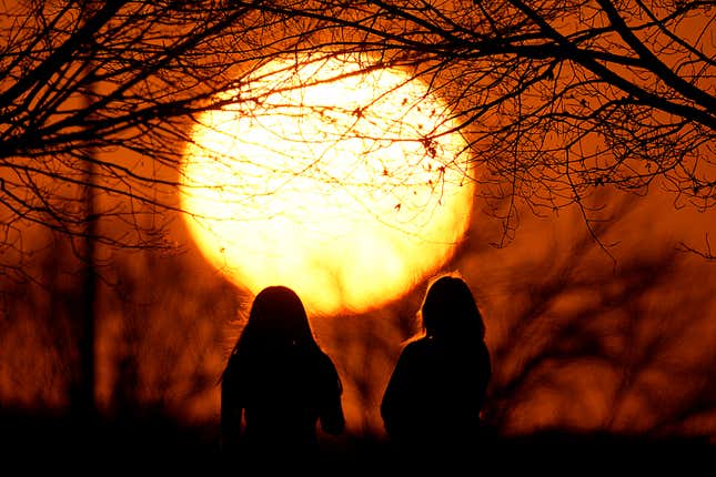 FILE - People watch the sunset at a park on an unseasonably warm day, Feb. 25, 2024, in Kansas City, Mo. A new study says climate change will reduce future global income by about 19% in the next 25 years compared to a fictional world that’s not warming. (AP Photo/Charlie Riedel, File)