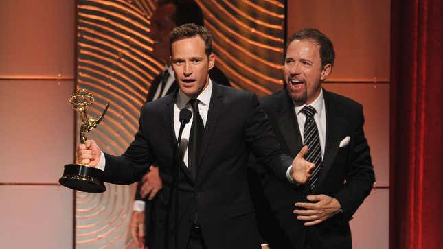 Mike Richards holding an Emmy award on stage.