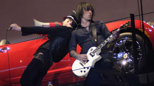 A photo of a band playing in front of a Saturn car. 