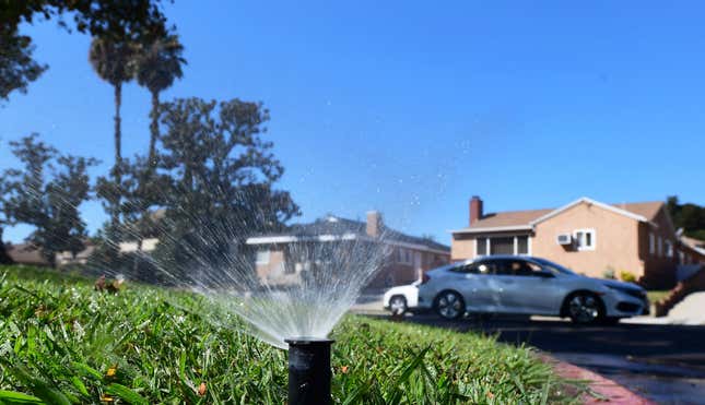 A sprinkler waters a green lawn in front of suburban houses.