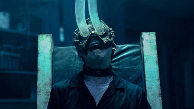 A person sits in a chair with a mask on that has hoses attached to the eye sockets.