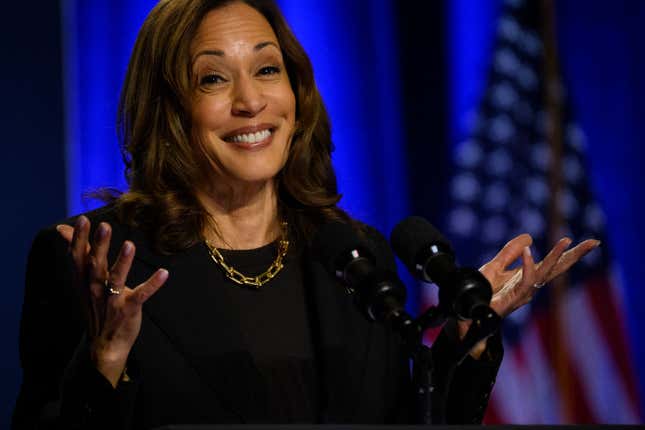 Vice President Kamala Harris, in all black, stands at a microphone while smiling